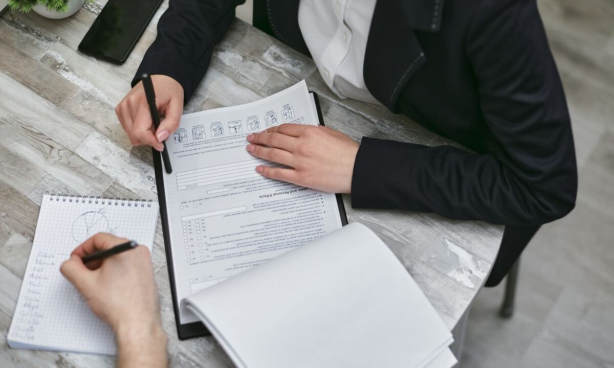 Pessoas revisando documentos e checklist de due diligence sobre uma mesa antes de fechar um negócio