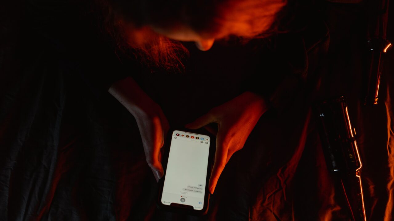 Mãos segurando um celular em ambiente escuro, representando o golpe do amor em apps de namoro
