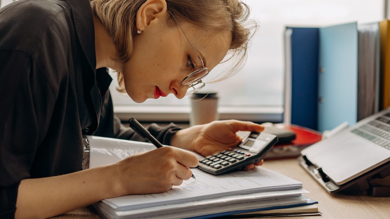 Mulher analisando documentos financeiros com calculadora, representando o cálculo e consulta do capital social de uma empresa