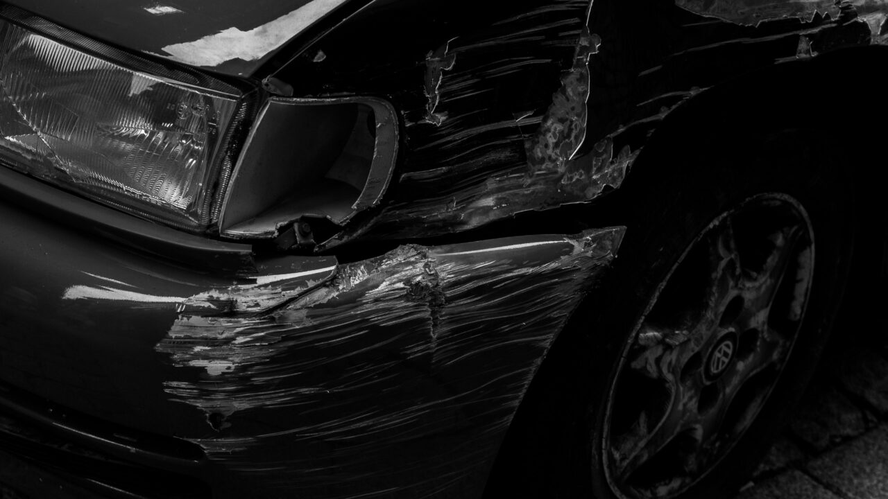 Lataria dianteira de um carro amassada e arranhada após uma colisão, em preto e branco