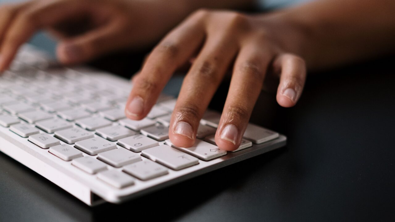 Mãos digitando em um teclado de computador, ilustrando a consulta ao novo formato alfanumérico do CNPJ