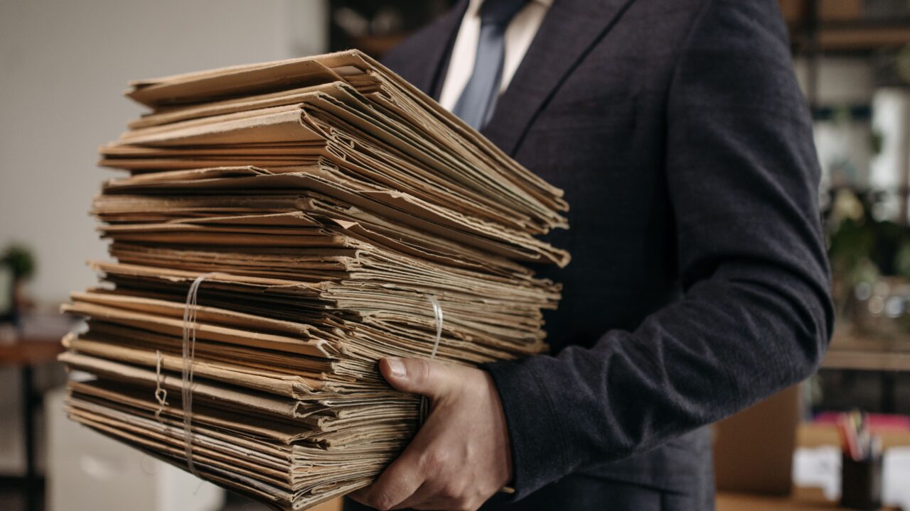 Homem de terno carregando pilha de pastas de documentos, representando regularização cadastral de empresa