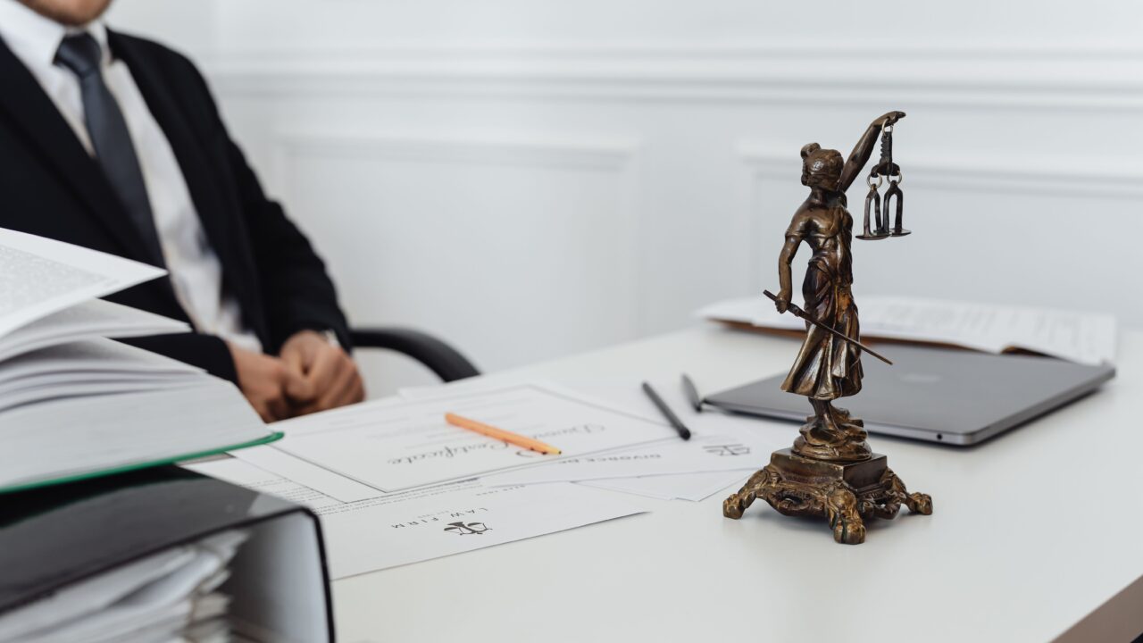 Advogado em escritório com documentos e uma pequena estatueta da balança da Justiça sobre a mesa