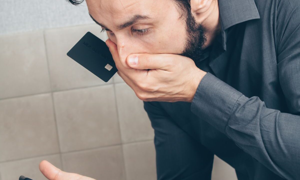 Homem com expressão preocupada segurando um cartão escuro perto do rosto, representando alerta sobre golpe de empréstimo falso