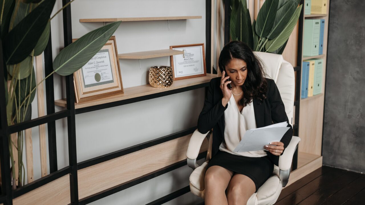 Mulher em ambiente de escritório falando ao telefone enquanto lê um documento, representando o pedido de explicação sobre o score de crédito