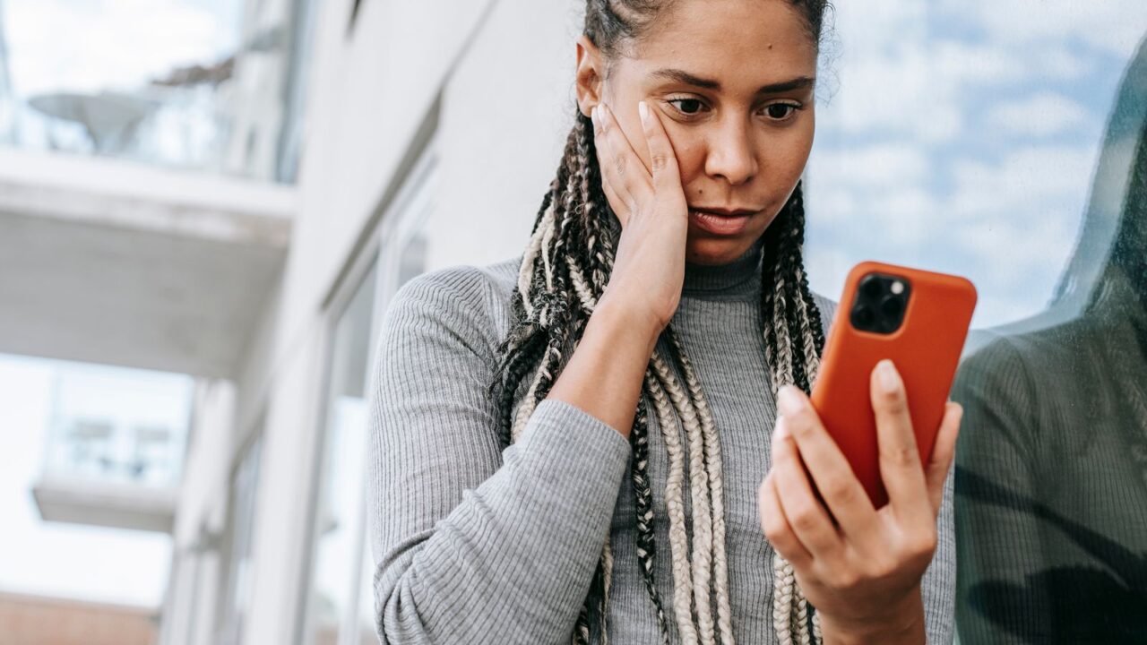 Mulher segurando o celular com expressão de atenção, verificando dados antes de confirmar uma transferência por Pix