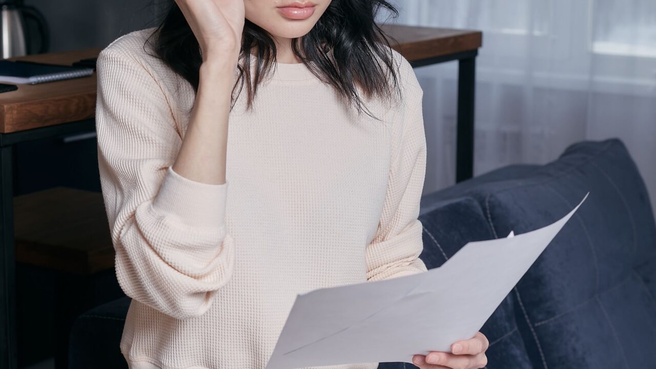 Mulher segurando óculos e lendo um documento de cobrança com expressão preocupada