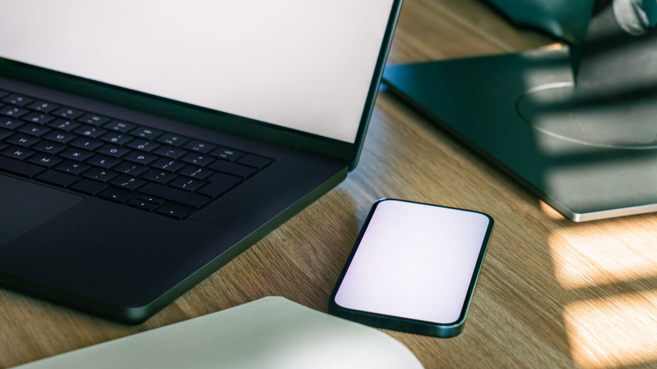 Laptop e smartphone lado a lado sobre uma mesa de madeira, simbolizando a conexão de dados entre instituições financeiras no Open Finance