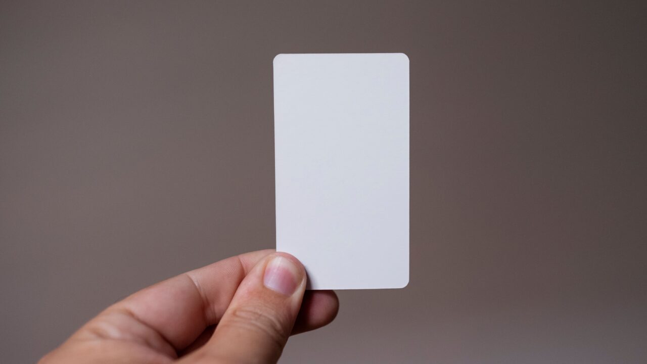 Mão segurando um cartão retangular em branco contra fundo neutro