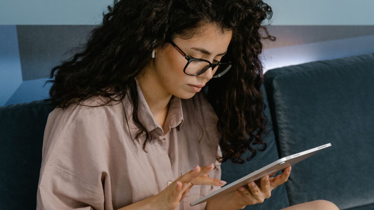 Mulher sentada no sofá usando um tablet para consultar seus dados financeiros online