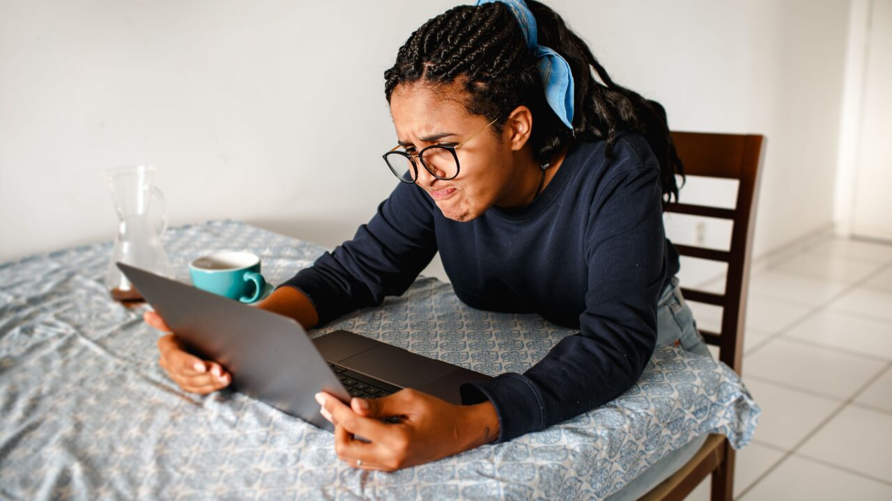 Mulher com expressão confusa olhando para a tela de um laptop em casa, representando a dúvida sobre por que o score de crédito caiu