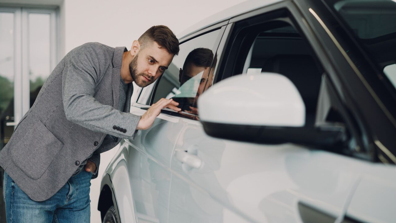 Homem inspecionando um carro branco de perto antes de fechar a compra de um veículo usado